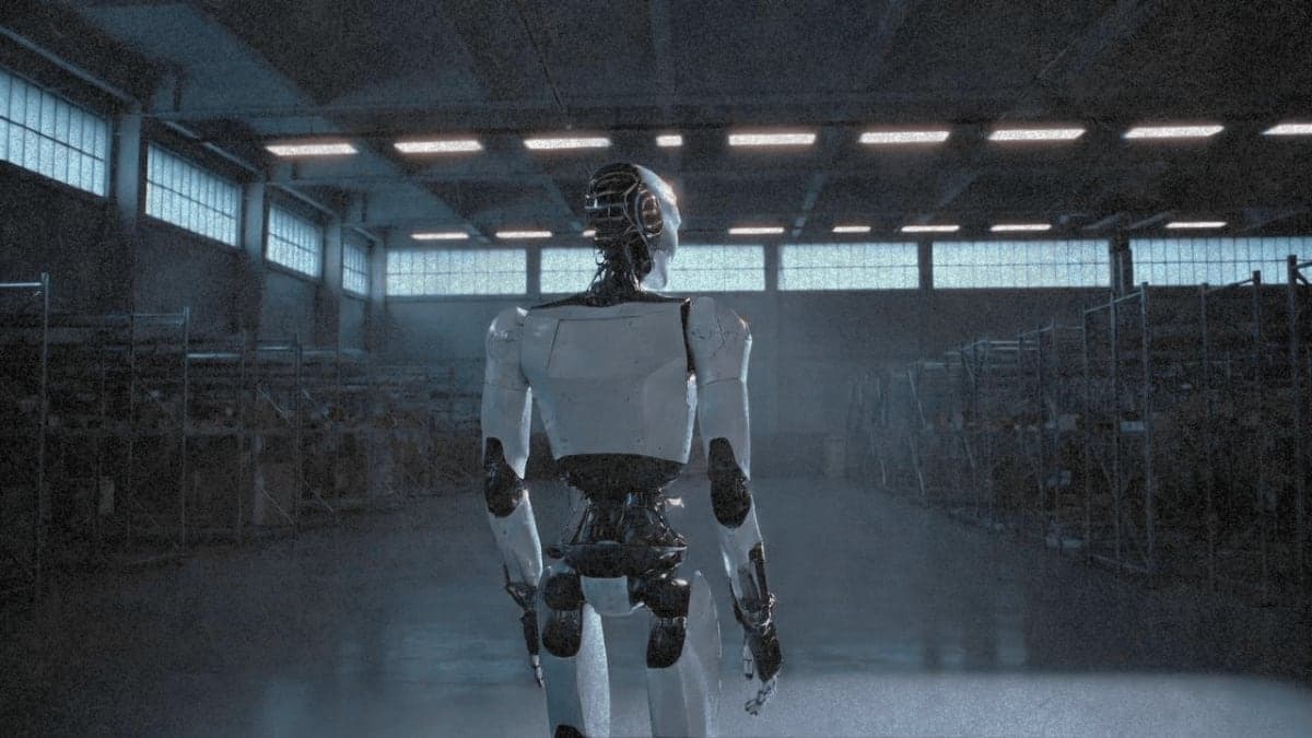 A humanoid robot stands alone in a modern warehouse at dawn, its white chassis illuminated by cool blue light from industrial windows, with empty shelving rows extending into the shadowed distance.