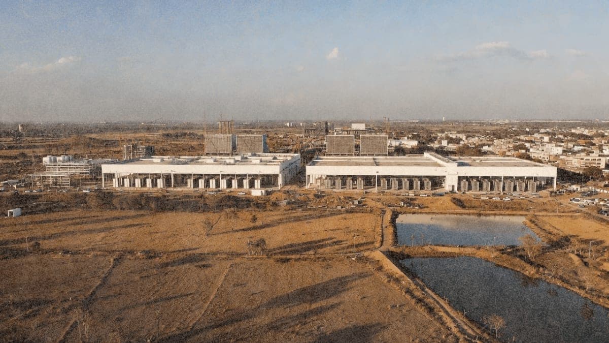 Modern data center under construction in India with cooling towers rising above traditional buildings and dried agricultural land in the foreground