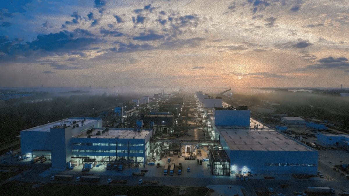 Aerial view of a large semiconductor manufacturing facility at dusk with cleanroom lighting visible through windows