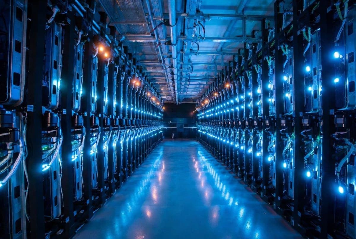 Rows of illuminated server racks stretching into the distance inside a massive data center, with cooling systems visible overhead
