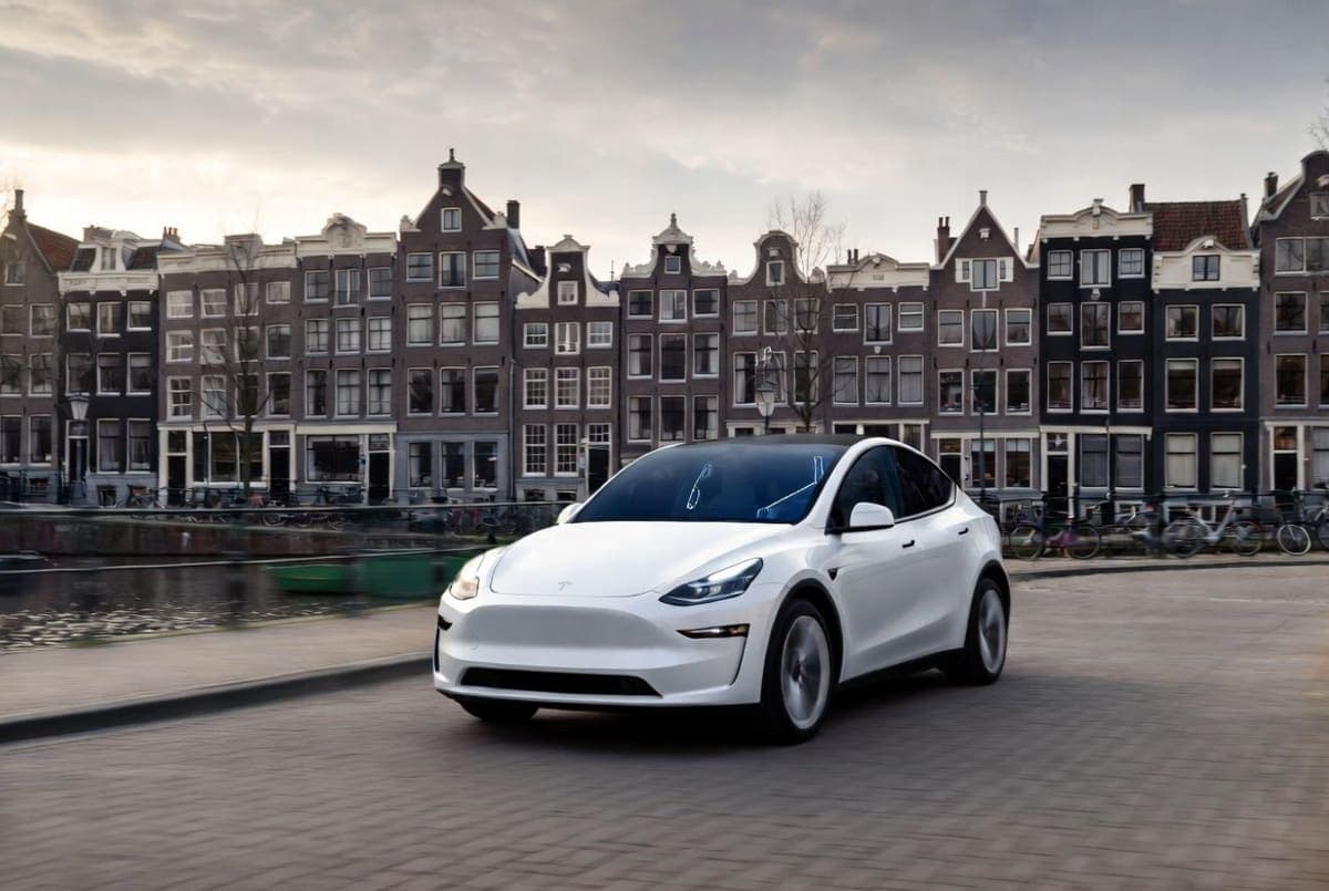 A Tesla vehicle navigating a Dutch city street with canal houses and cyclists in the background