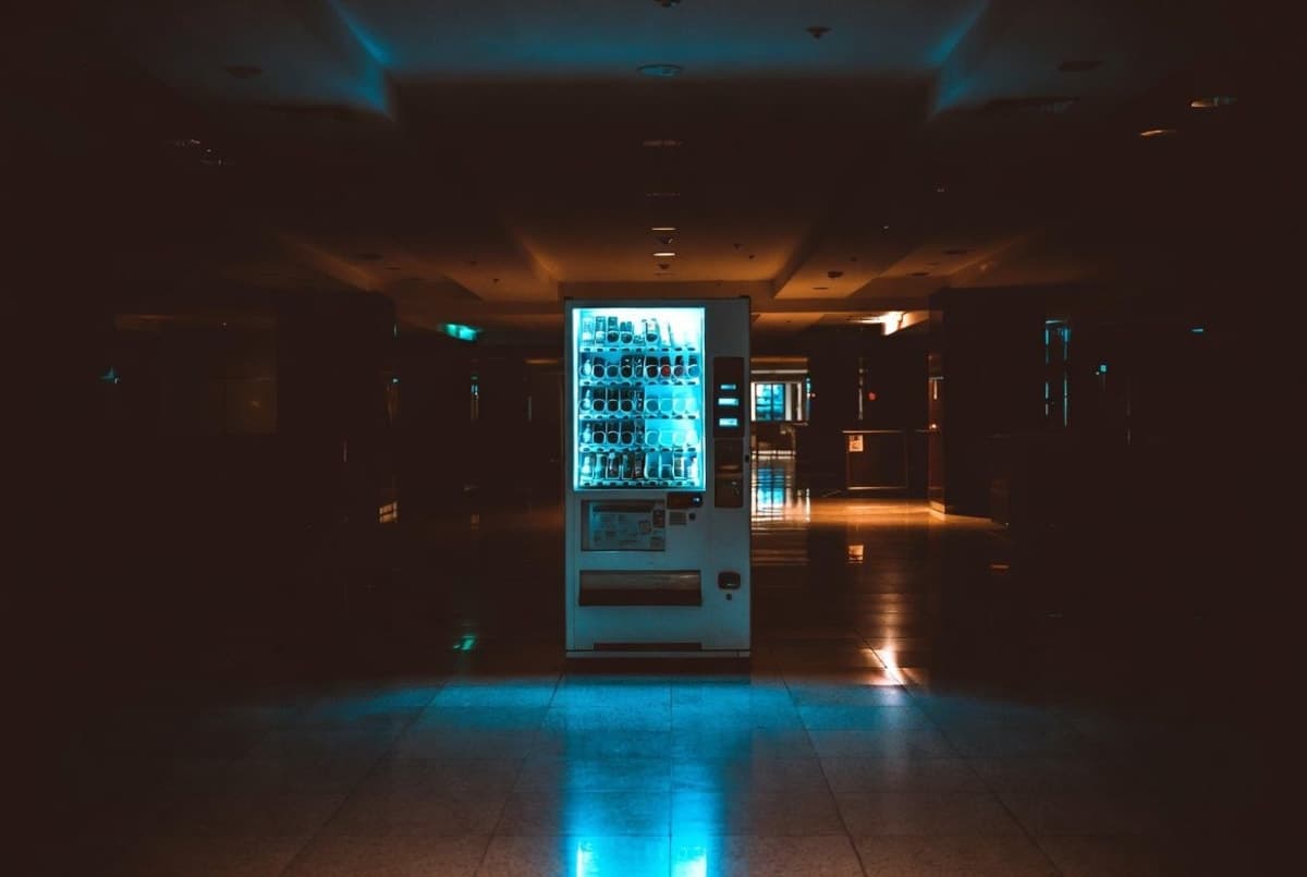 A lone vending machine glowing in a darkened office lobby at night, reflections on polished floor tiles