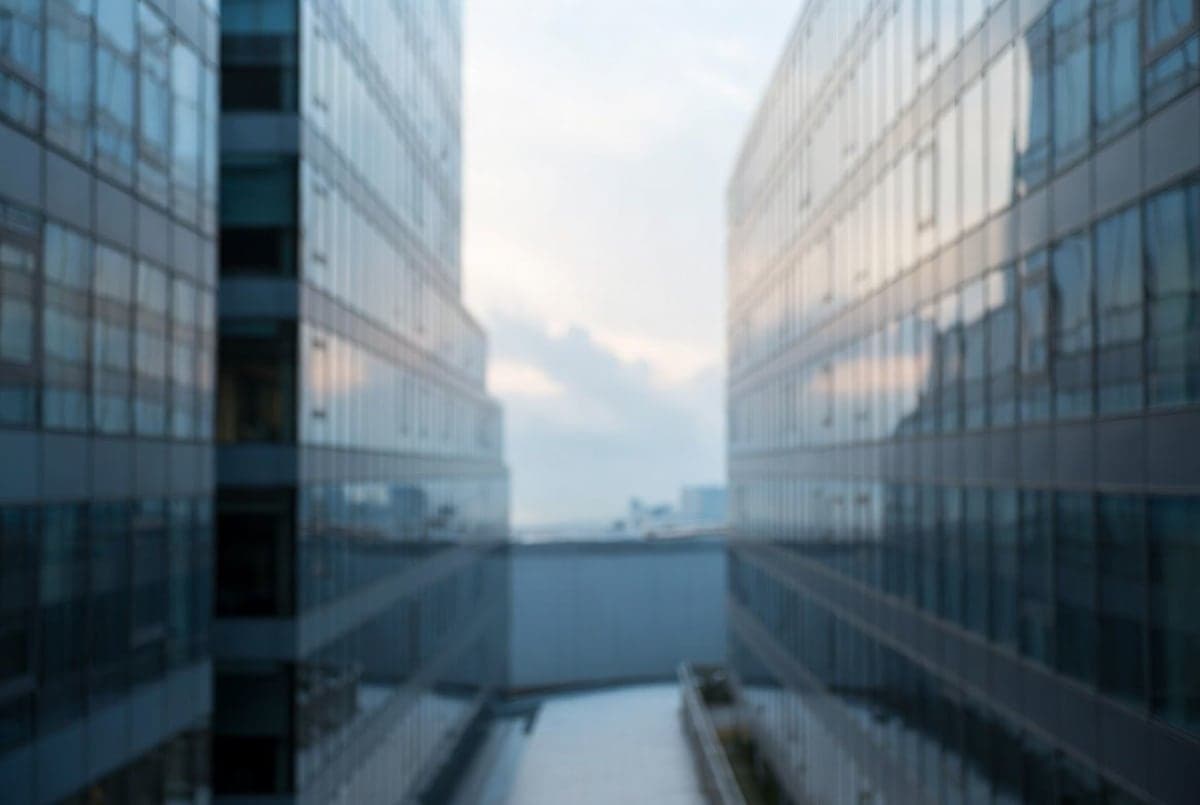 Two corporate office buildings facing each other across a divided horizon under cool blue light, suggesting a partnership shift