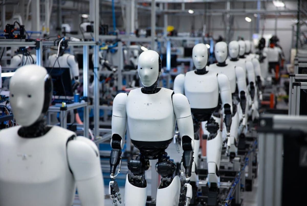White humanoid robots being assembled along a production line at a robotics manufacturing facility