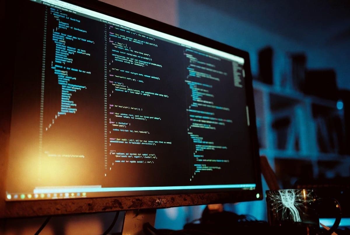 Developer's monitor in a dim office showing source code mid-scroll with abstract neural network reflections