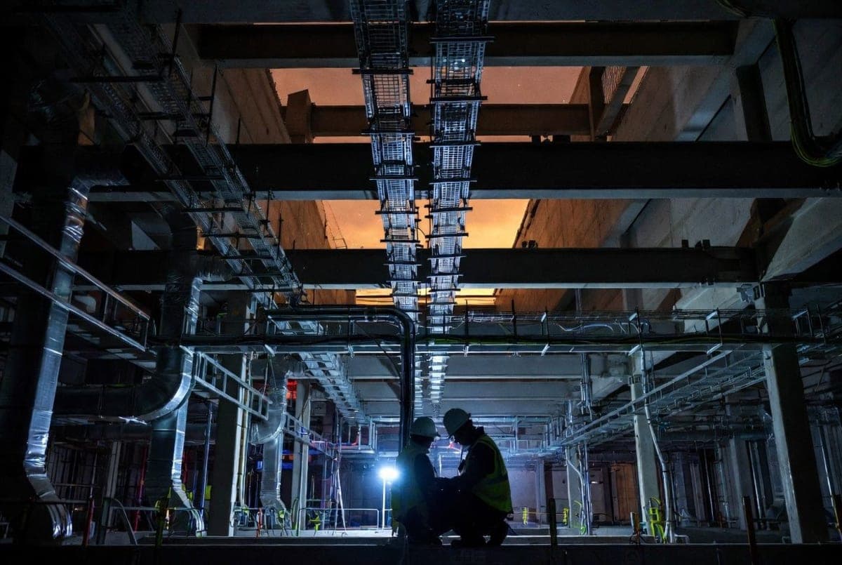 Construction workers installing electrical conduit and cooling infrastructure inside a partially built data center hall