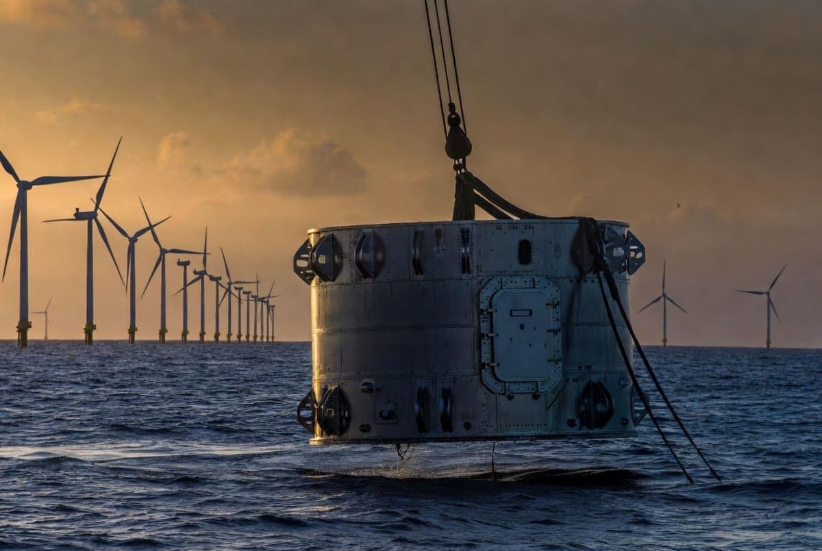 Sealed cylindrical server module being lowered into the sea beside offshore wind turbines