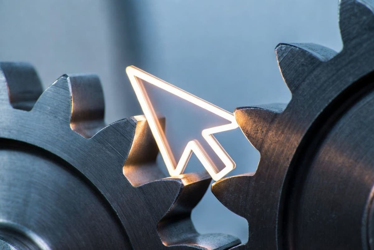 A cursor arrow wedged between large interlocking metal gears, representing AI agents in office workflows