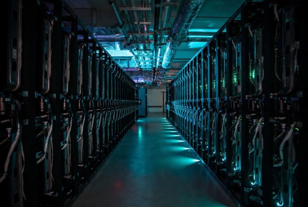 Rows of server racks inside a large data center with cooling infrastructure and blue indicator lights
