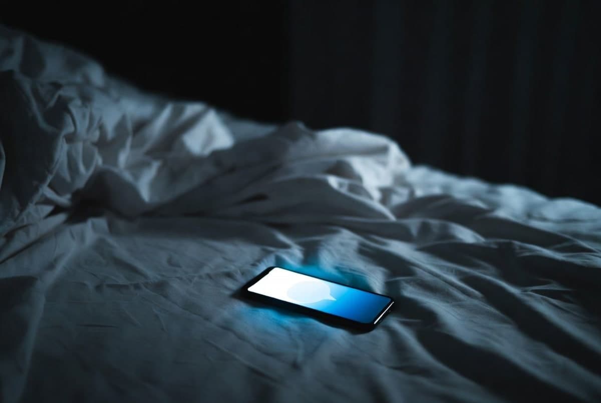 Smartphone glowing in a dark room with a chat interface, suggesting late-night conversation with an AI companion
